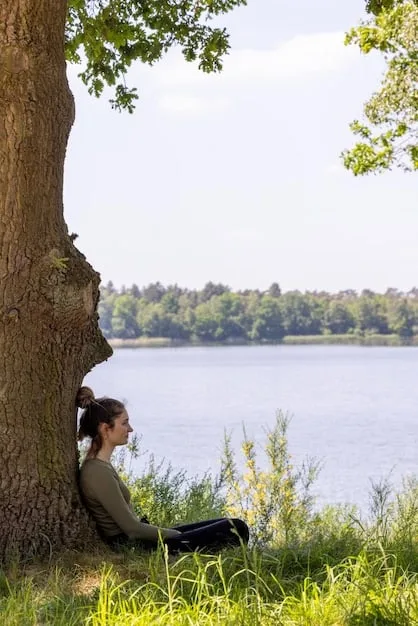 A person meditating in a peaceful setting, representing mindfulness and self-awareness. Sunlight streams through the trees, creating a serene atmosphere.
