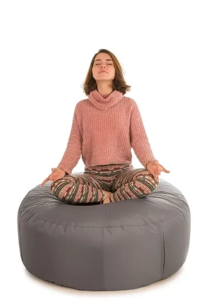 A person sitting cross-legged on a meditation cushion, eyes closed, with a gentle smile, focusing on their breath and practicing mindfulness.