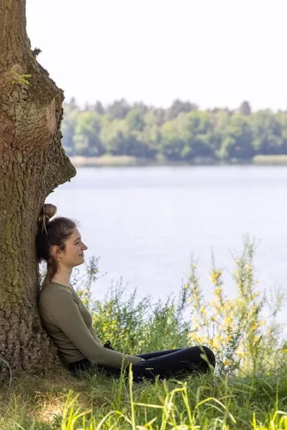 A person meditating in a peaceful setting, with sunlight filtering through the trees. Their eyes are closed, and they have a serene expression on their face, symbolizing self-compassion and inner peace.