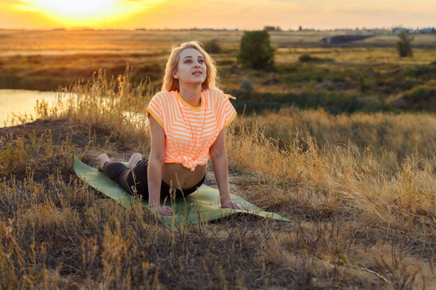 A person practicing yoga outdoors at sunrise, with a serene expression. The background shows a peaceful landscape, emphasizing the connection between physical activity, mindfulness, and emotional well-being.
