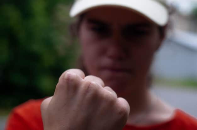 A close-up of a person clenching their fists tightly, with a blurred background suggesting a stressful environment, highlighting physical tension related to anger.