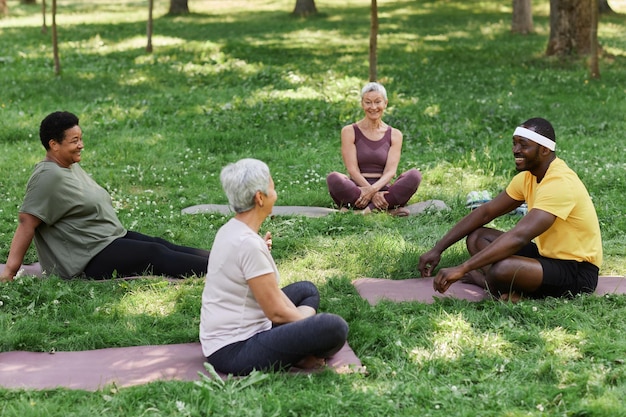 A diverse group of people practicing yoga outdoors in a park, surrounded by trees and greenery. They are performing various yoga poses, demonstrating flexibility and balance.