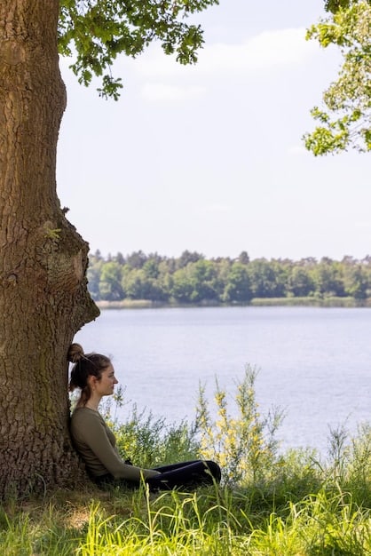 A person meditating in a peaceful setting, representing mindfulness and self-awareness. Sunlight streams through the trees, creating a serene atmosphere.