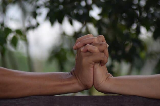 Two hands clasped together, symbolizing forgiveness and reconciliation, set against a blurred background of a peaceful garden.