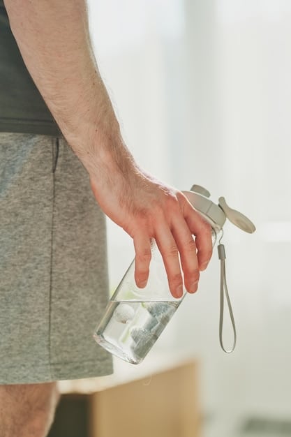 A close-up of a person's hand reaching for a water bottle during a workout. The background is blurred to focus on the action, emphasizing the importance of hydration during physical activity. The bottle is partially transparent, showing the refreshing water inside.